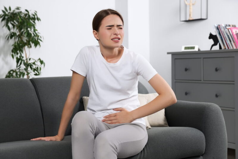 Young woman suffering from cystitis on sofa at home